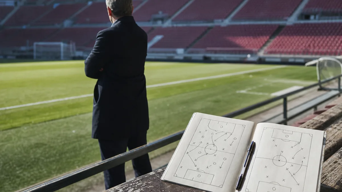Football coach in a suit by the touchline in a modern stadium, giving instructions with a focused gesture